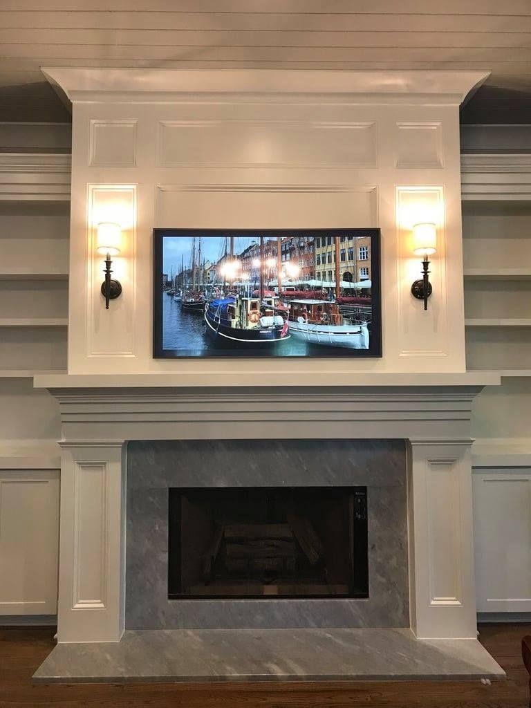 Modern living room fireplace with white mantel and a wall-mounted TV showing a city harbor scene