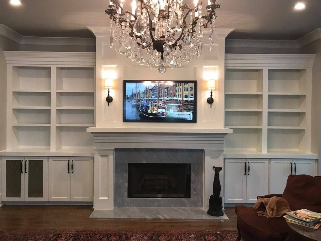 Elegant living room with white built-in shelves, a fireplace, chandelier, and wall-mounted TV