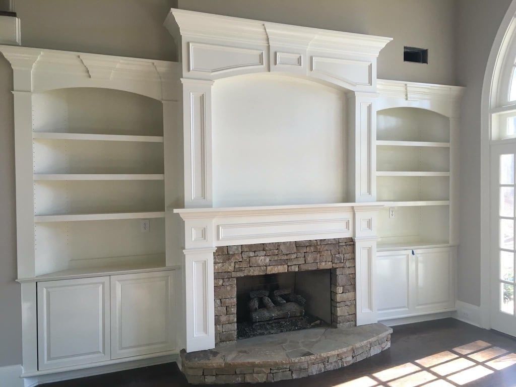Built-in white cabinets and bookshelves flanking a fireplace with a stone surround in a bright living room