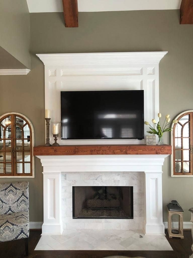 Living room fireplace with large wall-mounted TV, white mantel, and decorative mirrors on both sides
