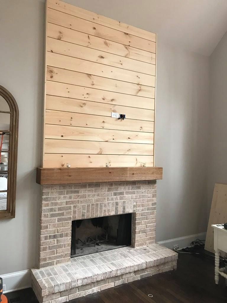 Corner fireplace with a white brick hearth and tall unfinished wood panel above it.