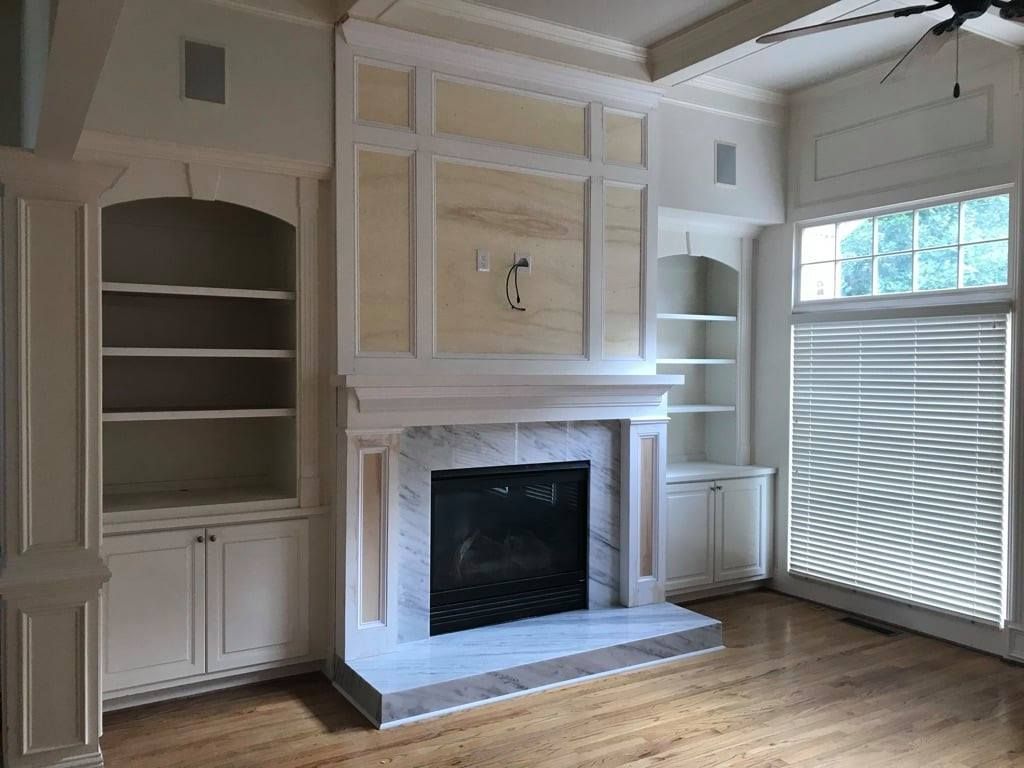Living room with built-in shelves, a white fireplace, and a large window with blinds