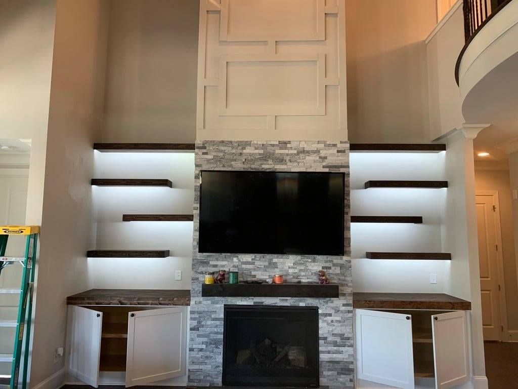 Living room fireplace wall with built-in shelves, TV, and stone surround