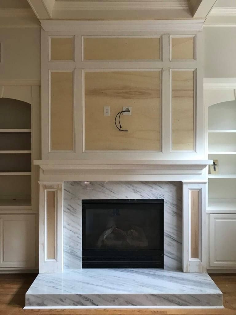 Built-in fireplace with white marble surround and unfinished beige paneled wall above.