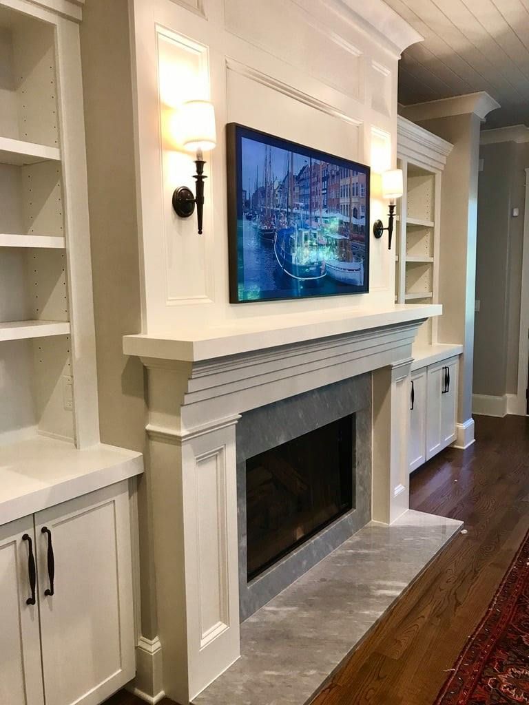 Elegant white living room with a wall-mounted TV above a fireplace and built-in cabinets