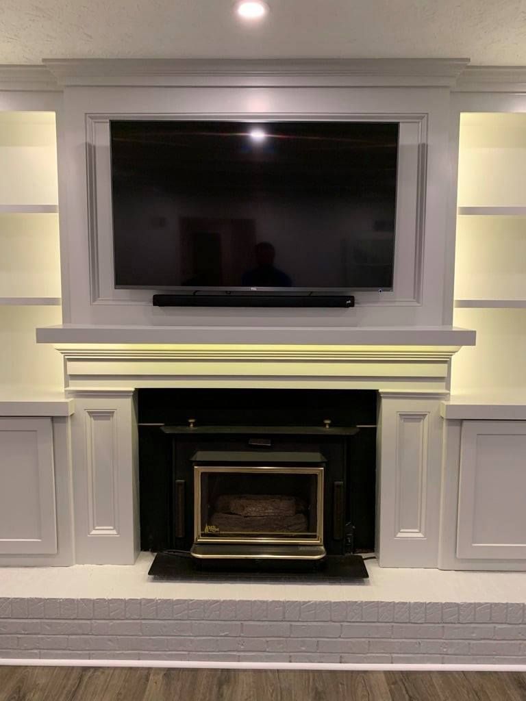Built-in TV above a fireplace with gray paneled cabinetry and recessed shelves