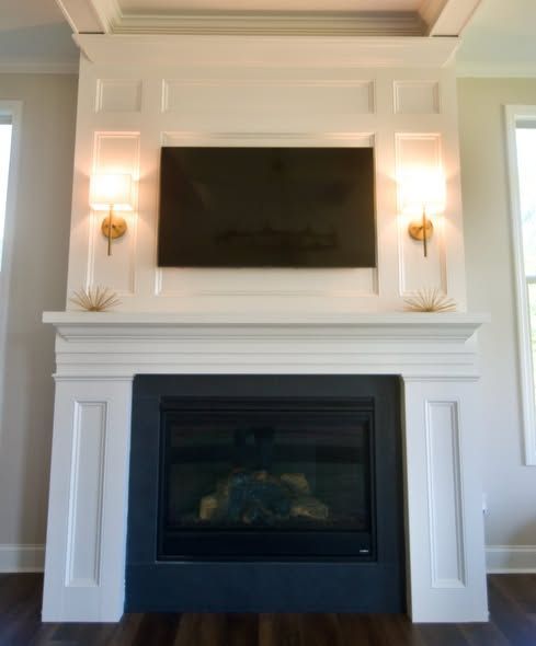 Modern white fireplace with a mounted TV and wall sconces above a black firebox