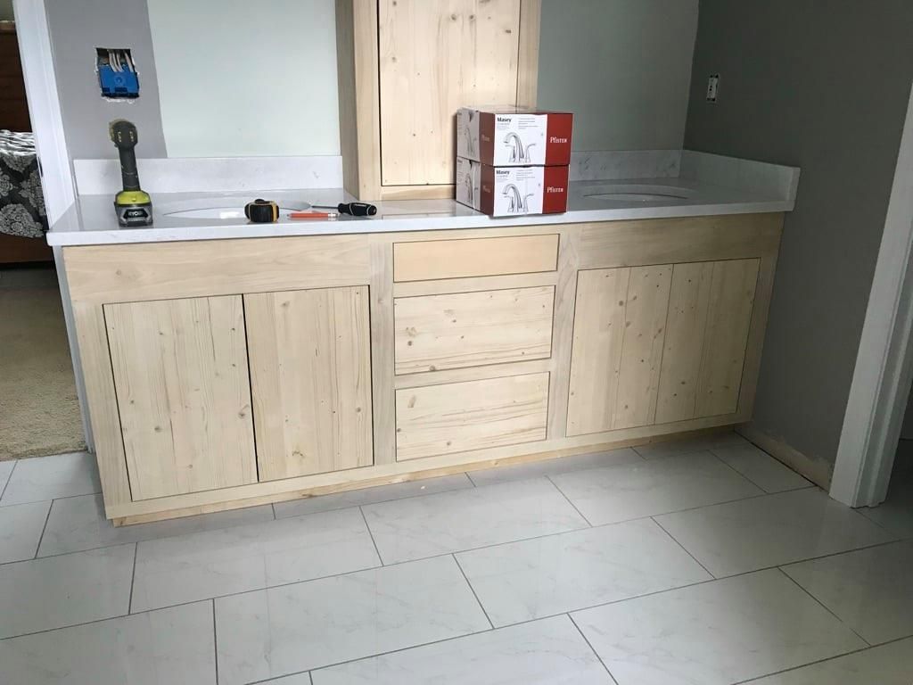 Kitchen with light wood cabinets, gray countertop, and a few items on top in a tiled room.