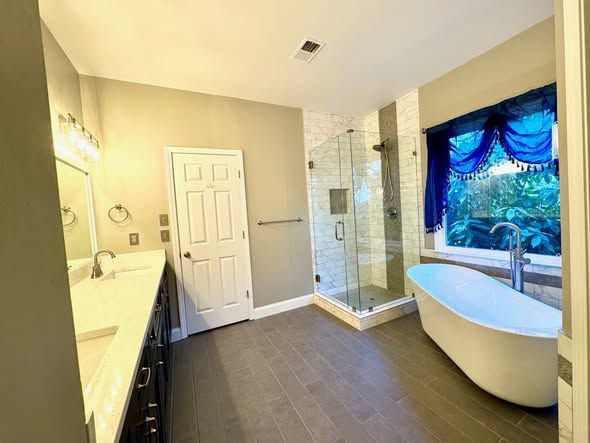 Bright bathroom with vanity, shower, freestanding tub, and large window with blue curtain.