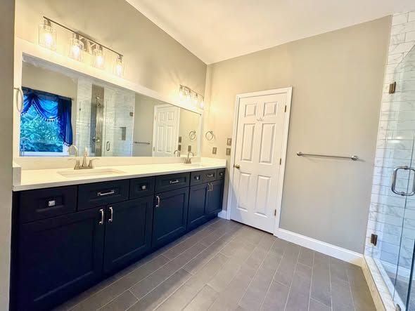 Modern bathroom with dark vanity, double sinks, large mirror, and walk-in shower