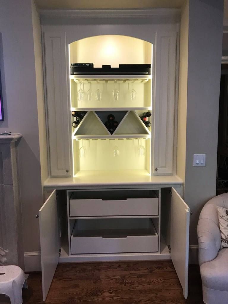 Built-in white shelving unit with warm lights and cabinet doors in a living room alcove