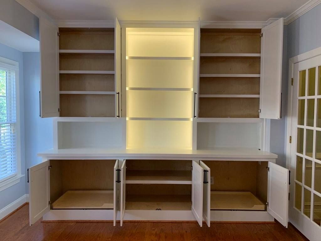 Built-in white shelving and cabinets in a bright room, with open upper shelves and lower storage compartments.
