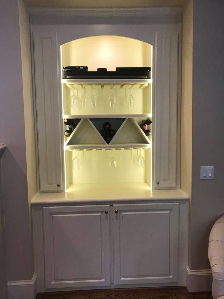Built-in wall cabinet with lit shelves and mirrored back, framed by white trim and lower storage doors.