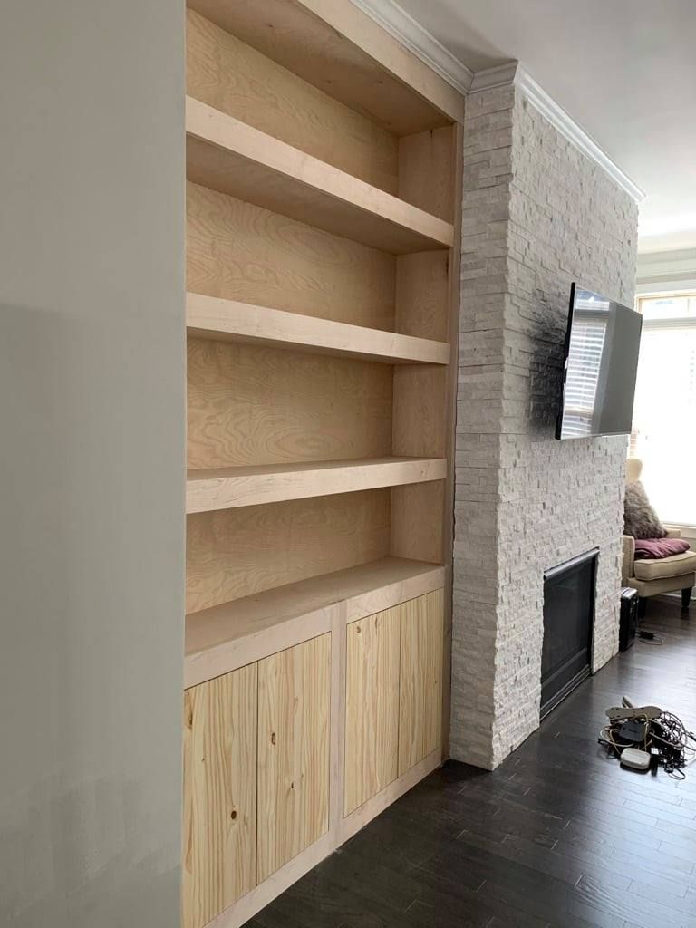 Built-in wood shelves beside a white stone fireplace in a modern living room.