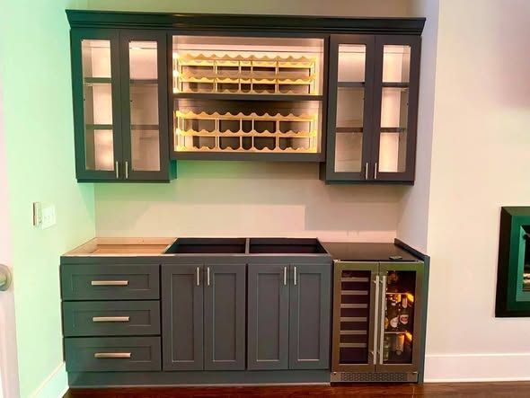 Wall-mounted black bar cabinet with glass doors, shelves, drawers, and a wine cooler against a white wall.