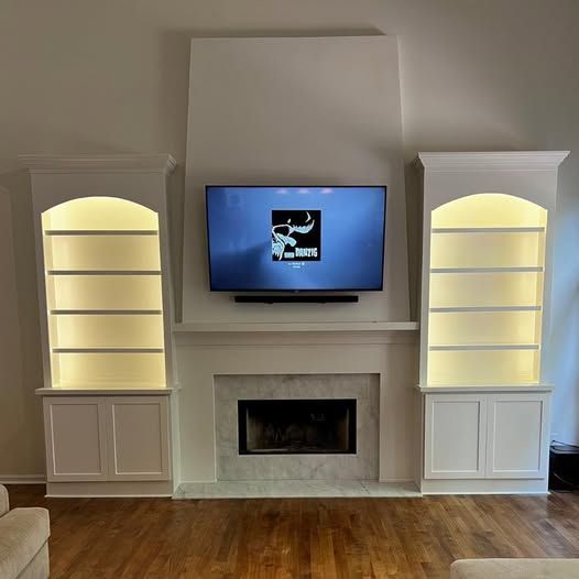 Modern living room with built-in cabinets, a TV above a fireplace, and warm-lit display shelves