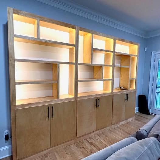 Built-in wooden shelving unit with warm backlighting above closed cabinets in a living room