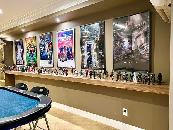 Framed movie posters and collectible figures displayed on a shelf in a home game room