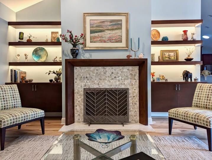 Living room with a fireplace, built-in shelves, patterned chairs, and framed art