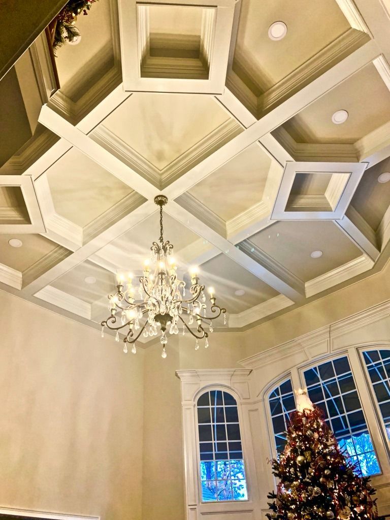 Elegant coffered ceiling with chandelier above a decorated Christmas tree by arched windows