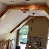 Vaulted living room ceiling with exposed wood beams, recessed lights, and a hanging pendant light above an arched window.