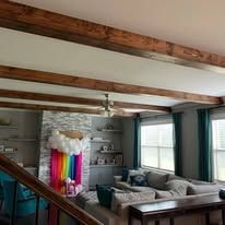 Living room with exposed wood beams, gray sectional sofa, teal curtains, and colorful hanging fabric display