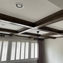 Living room ceiling with dark wood beams, recessed lights, and window shutters below