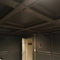 Dim room with dark paneled walls, coffered ceiling, and an open white door.