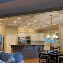 Open-plan kitchen and dining room with white cabinets, dark island, pendant lights, and blue sofa in foreground