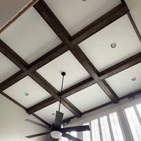Ceiling with dark wooden beams, white panels, recessed lights, and a black ceiling fan near a window.