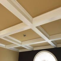 Beige coffered ceiling with white beams and a round window below.