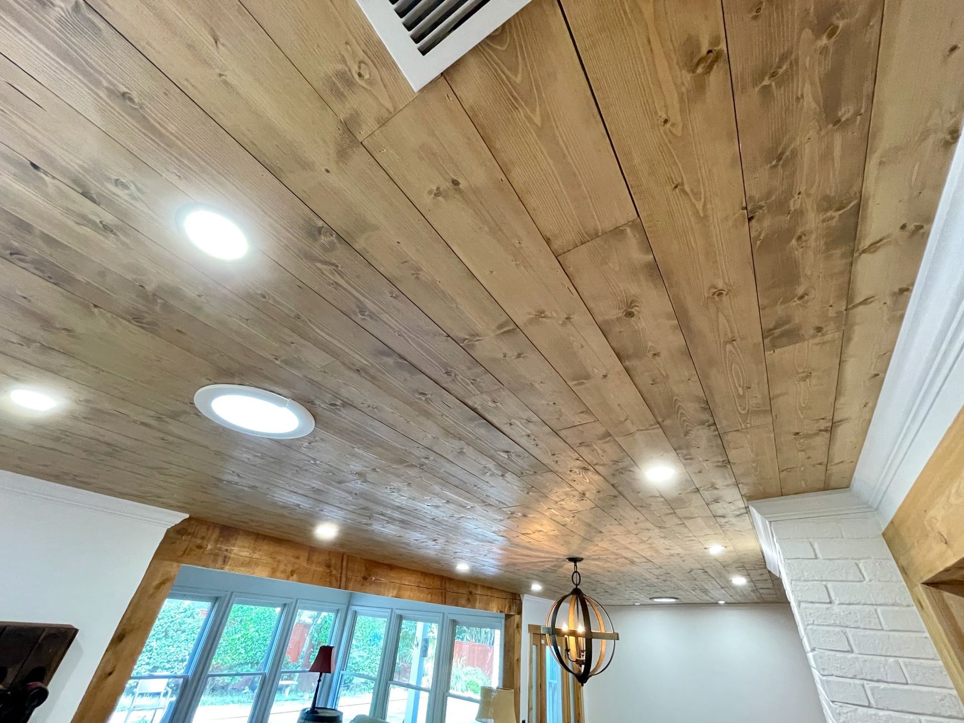 Wood-paneled ceiling with recessed lights, skylights, and a hanging lantern above a bright room