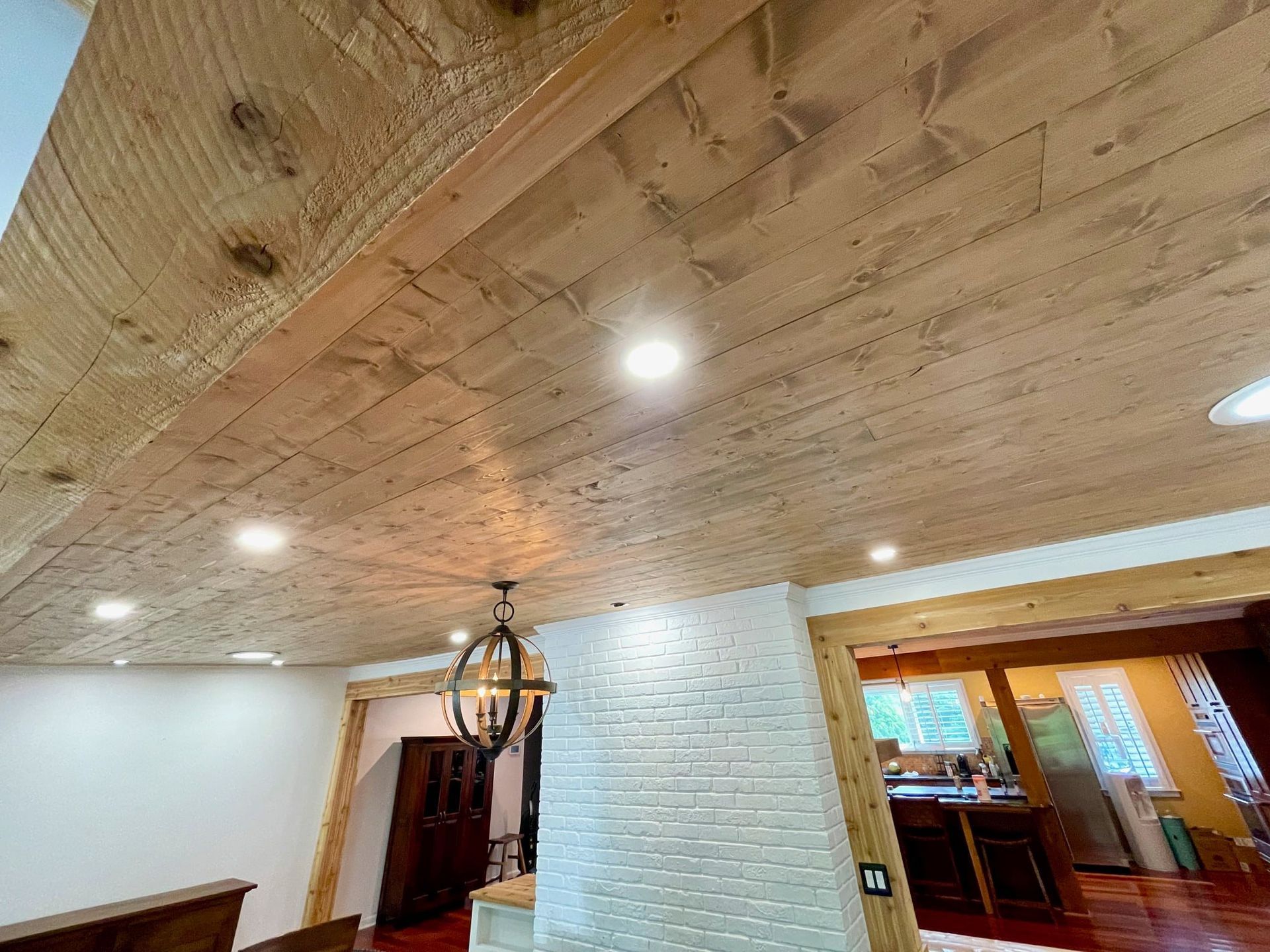 Wood-paneled vaulted ceiling with recessed lights above an indoor living space and doorway.