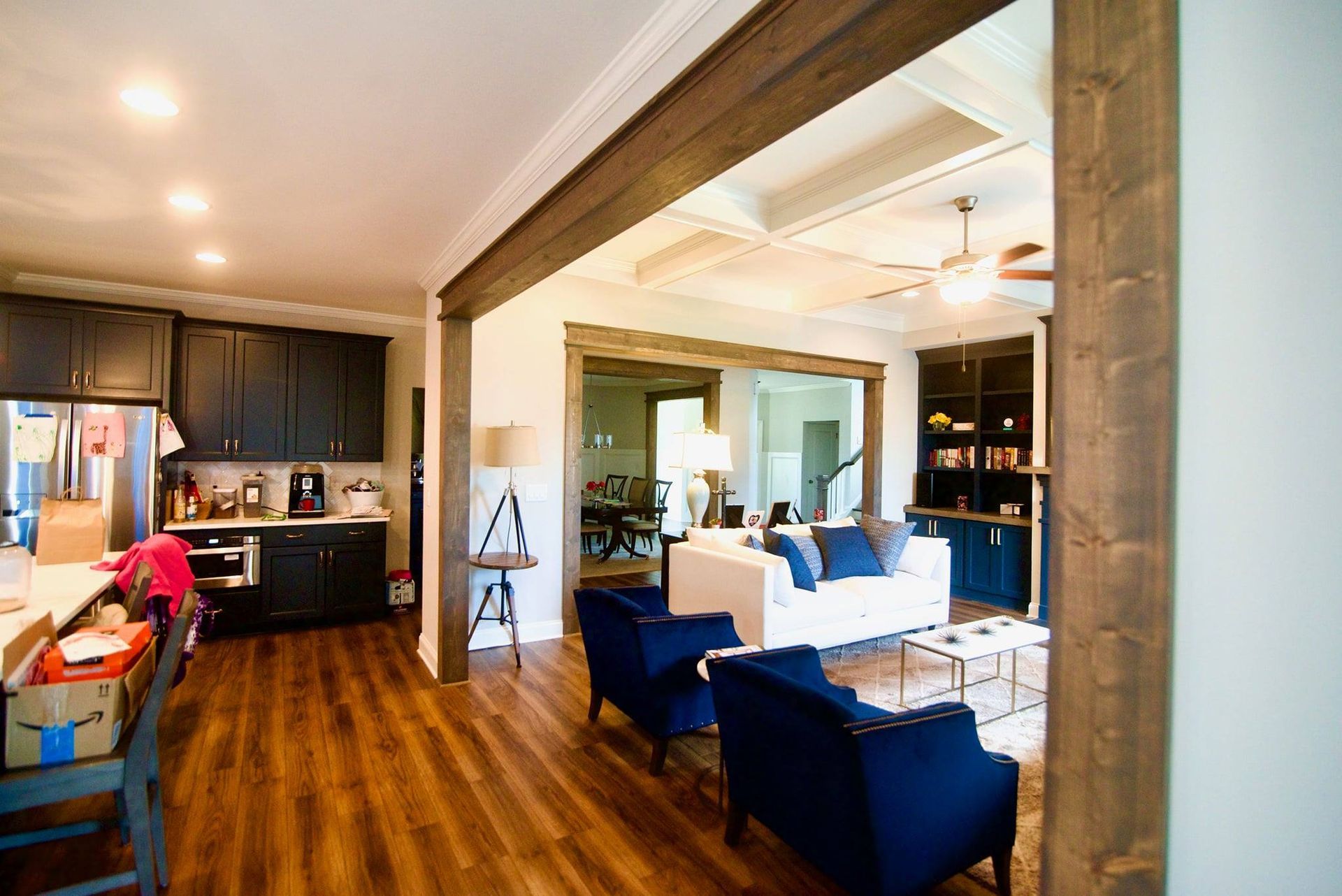 Modern living room with blue chairs, white sofa, wood floors, and kitchen in the background
