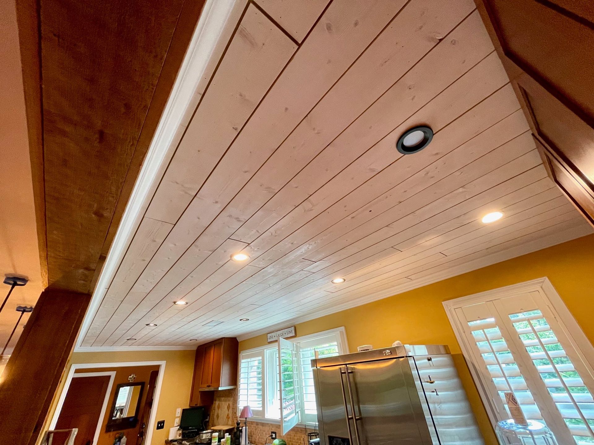 Warm kitchen interior with wood ceiling, recessed lights, windows, and a metal storage rack