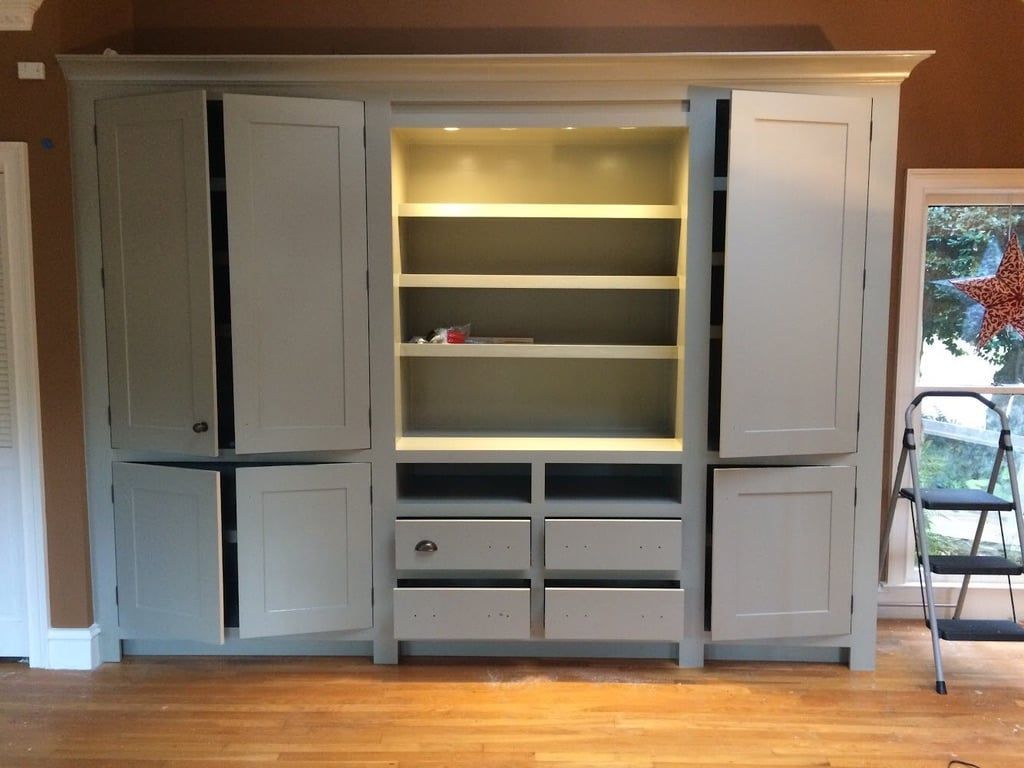 Built-in gray cabinets with shelves and drawers in a wood-paneled room, lit by warm recessed lighting