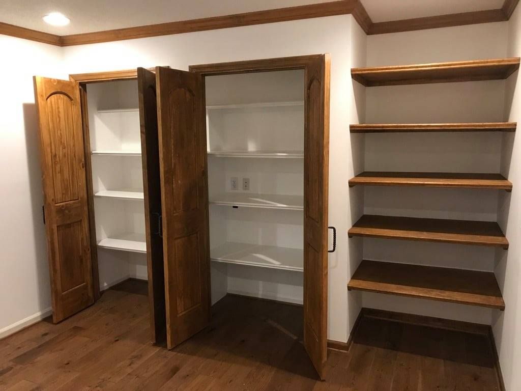 Walk-in closet with open wooden cabinet doors, white shelves, and a built-in shelving unit on the right.