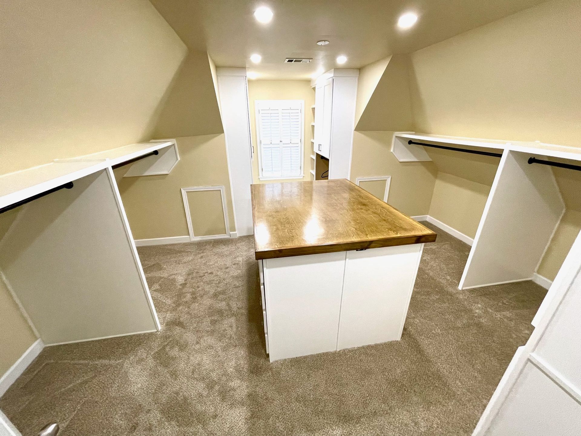 Small walk-in closet with built-in shelves, white cabinets, beige carpet, and a central wooden island.