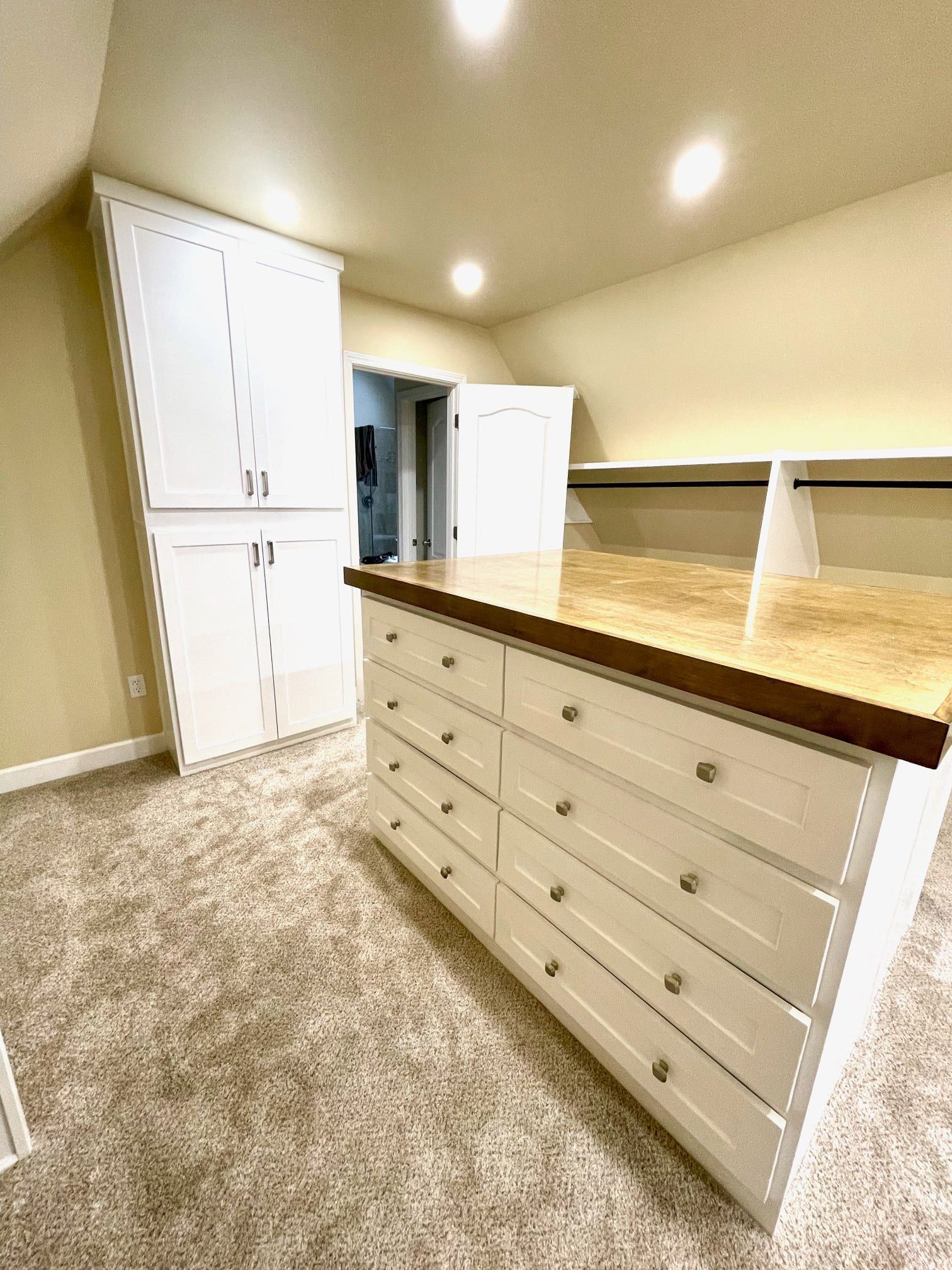 Bright walk-in closet with white drawers, built-in cabinets, beige carpet, and wood countertop.