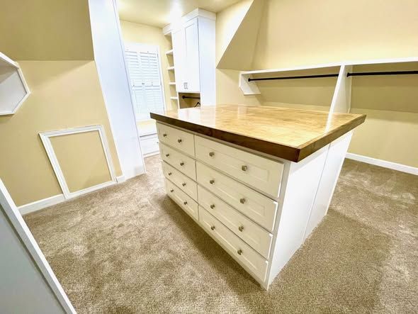 Walk-in closet with built-in drawers, white shelves, and beige carpet under a wood countertop island