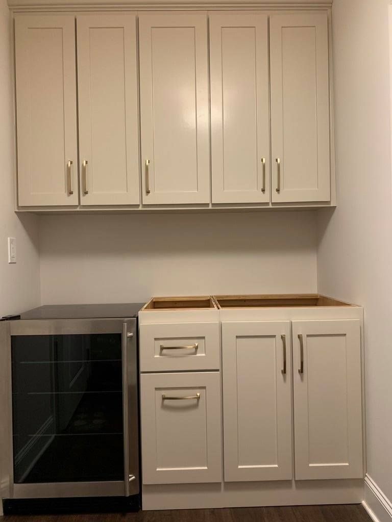 Kitchen cabinets above a countertop and sink, with a black beverage cooler on the left.