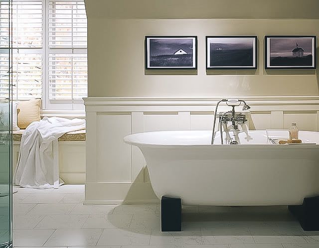 Bright bathroom with a freestanding tub, window seat, and framed landscape photos on the wall.