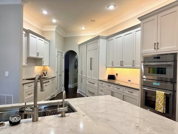 Bright modern kitchen with white cabinets, marble island, stainless appliances, and warm under-cabinet lighting.