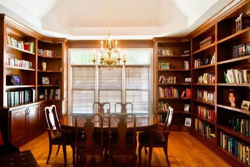 A wooden dining room featuring a table and chairs surrounded by floor-to-ceiling built-in bookshelves filled with books.