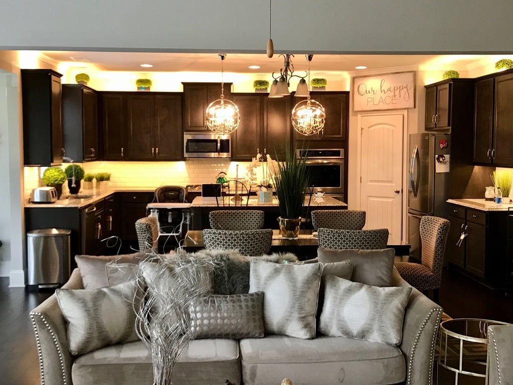 Open-concept kitchen and living room with dark cabinets, pendant lights, and a light-colored sofa.