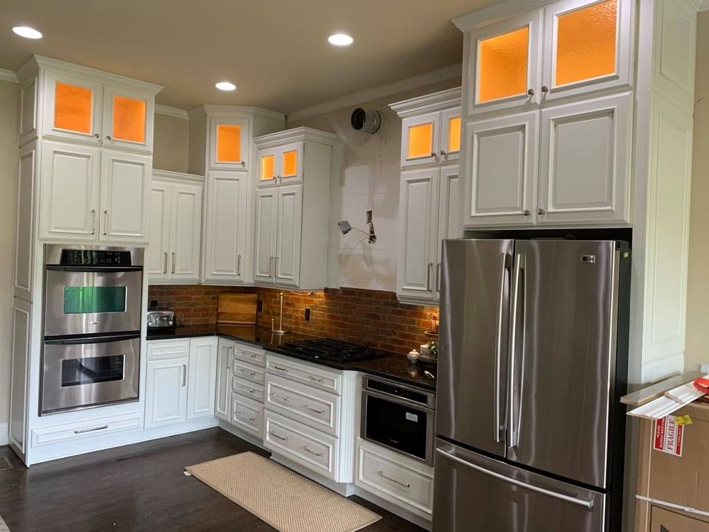 Bright white kitchen with stainless steel appliances, wood floors, and amber-lit cabinet windows