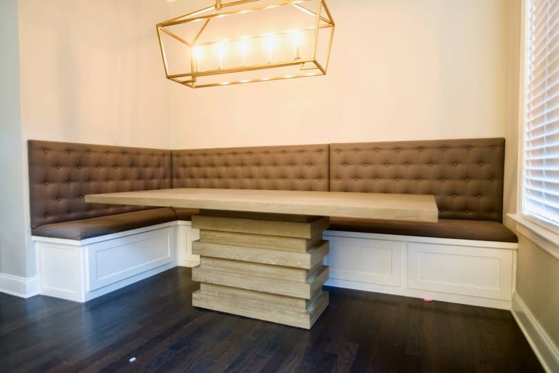 Modern dining nook with tufted bench seating, wooden table, and geometric pendant light on dark floors