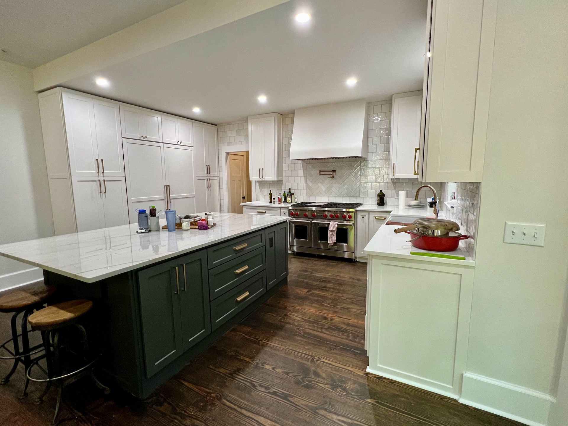 Bright kitchen with white cabinets, dark green island, marble counters, and stainless steel appliances