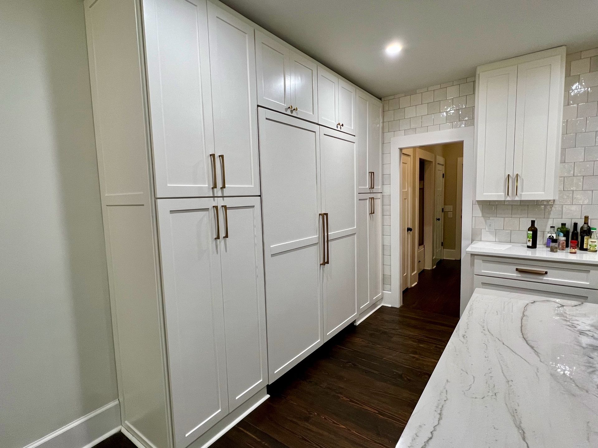 Bright kitchen hallway with white built-in cabinets, dark wood floor, and a countertop on the right.