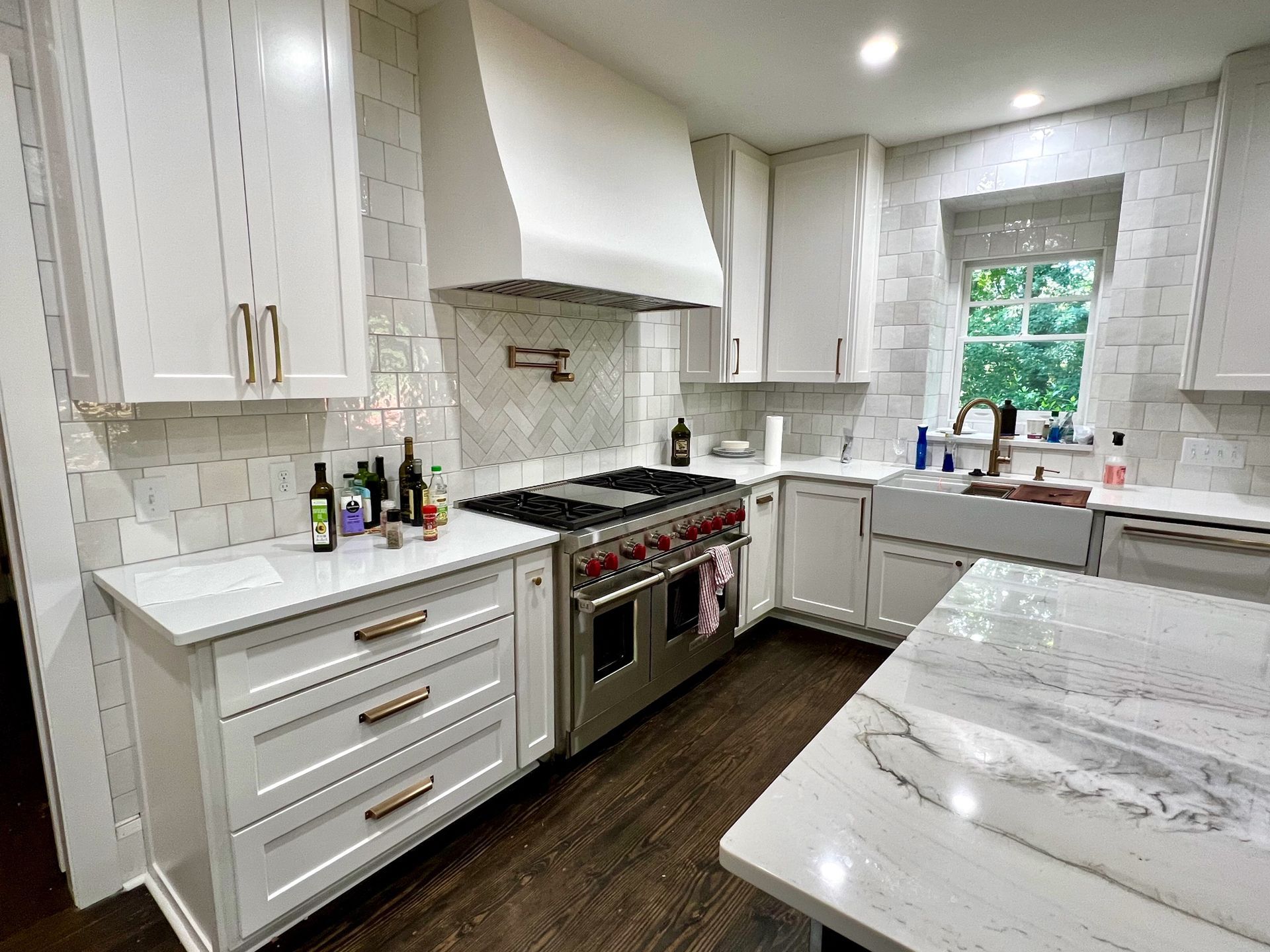 Bright white kitchen with marble counters, stainless stove, and window above the sink